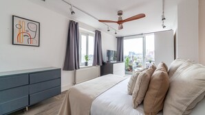 A modern bedroom with a bed, a dresser, a TV, and a city view. - The Nine Elms Collection (London)