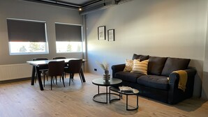 Uma sala de estar moderna com um sofá escuro, uma mesa de centro redonda e uma área de jantar com mesa e cadeiras.
