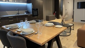 Uma sala de jantar moderna com uma mesa de madeira posta para quatro pessoas, com pratos, tigelas e copos brancos.