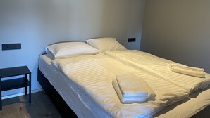 Cama bem arrumada com lençóis brancos e uma toalha dobrada ao lado.