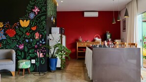 A modern kitchen with a central island, a dining area with wooden chairs, and a vibrant red accent wall. - Loft Rua Direita Você vai Adorar Este Lugar Único e Romântico (Centro Pirenópolis)