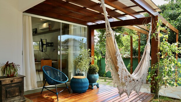 A wooden deck with a hammock, a blue chair, and potted plants. - Loft Rua Direita Você vai Adorar Este Lugar Único e Romântico (Centro Pirenópolis)