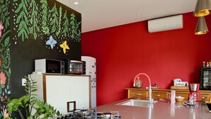 A modern kitchen with a red accent wall, a gas stove, a microwave, and a coffee maker. - Loft Rua Direita Você vai Adorar Este Lugar Único e Romântico (Centro Pirenópolis)