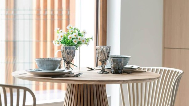 Ein runder Esstisch mit einer Blumenvase, zwei Gläsern und Tellern.