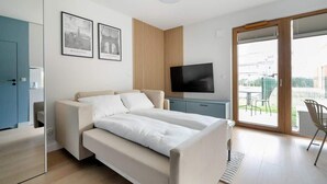 Ein modernes Schlafzimmer mit Schlafsofa, Flachbildfernseher und einer Glastür zum Außenbereich.