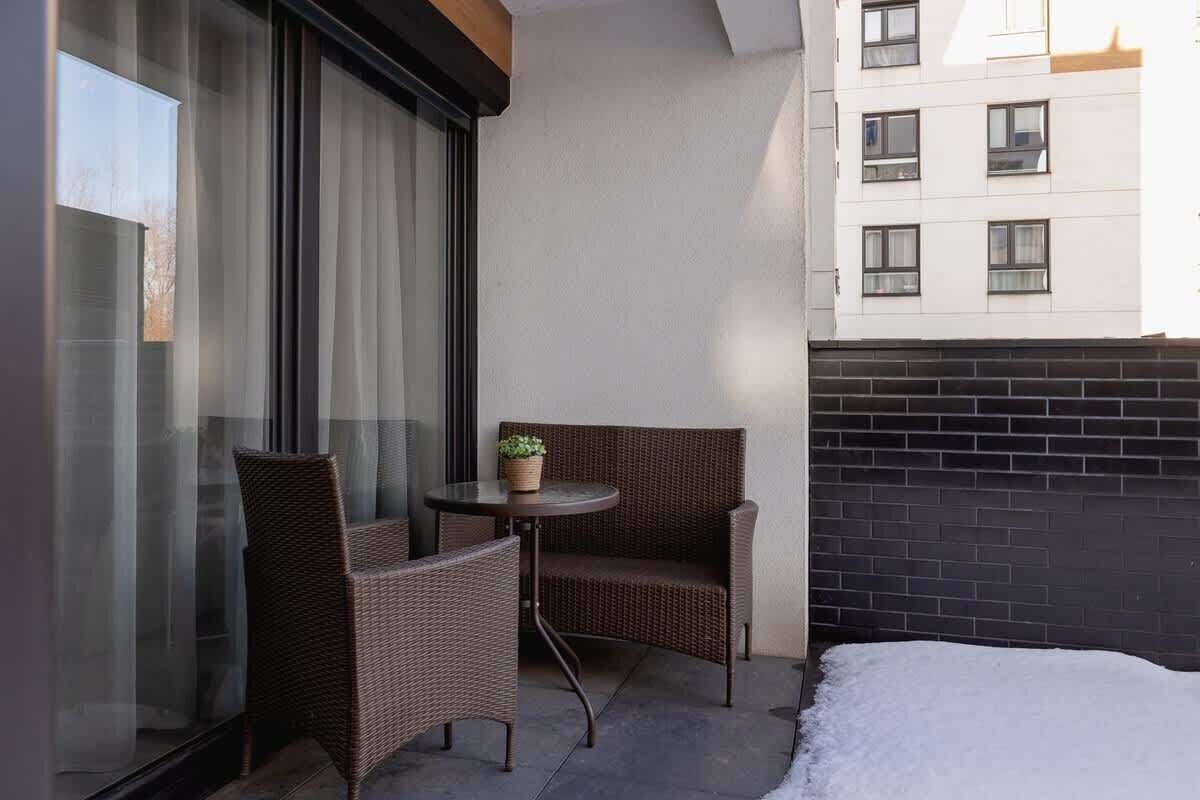 A balcony with wicker furniture, a small table with a plant, and a view of a building with multiple windows.