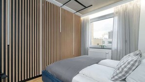 A modern bedroom with a bed, a wooden slat wall, and a window with curtains. - Stylish Apartment | Balcony (Poznan)