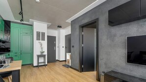 A modern living space with a dining area, a kitchen with green cabinets, a grey accent wall, and a large flat-screen TV mounted on the wall. - Stylish Apartment | Balcony (Poznan)