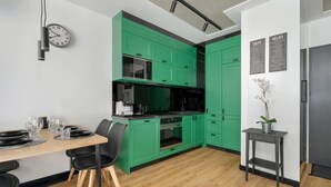 A modern kitchen with green cabinets, a wooden dining table, and black chairs. - Stylish Apartment | Balcony (Poznan)