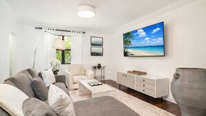 A modern living room with a grey sofa, a white armchair, a coffee table, a large TV, and a decorative pot.