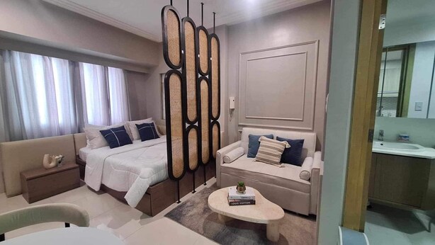 A modern hotel room with a large bed, a sofa, a small table, and a bathroom visible through an open door. - The Hamptons - a luxury Cebu Condo near Ayala (Cebu City)