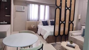 A modern hotel room with a round dining table, a sofa, a bed with a headboard, and a decorative wall panel. - The Hamptons - a luxury Cebu Condo near Ayala (Cebu City)