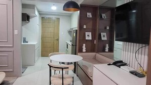 A modern living room with a round table and chairs, a sofa, a TV mounted on the wall, and a kitchen area in the background. - The Hamptons - a luxury Cebu Condo near Ayala (Cebu City)