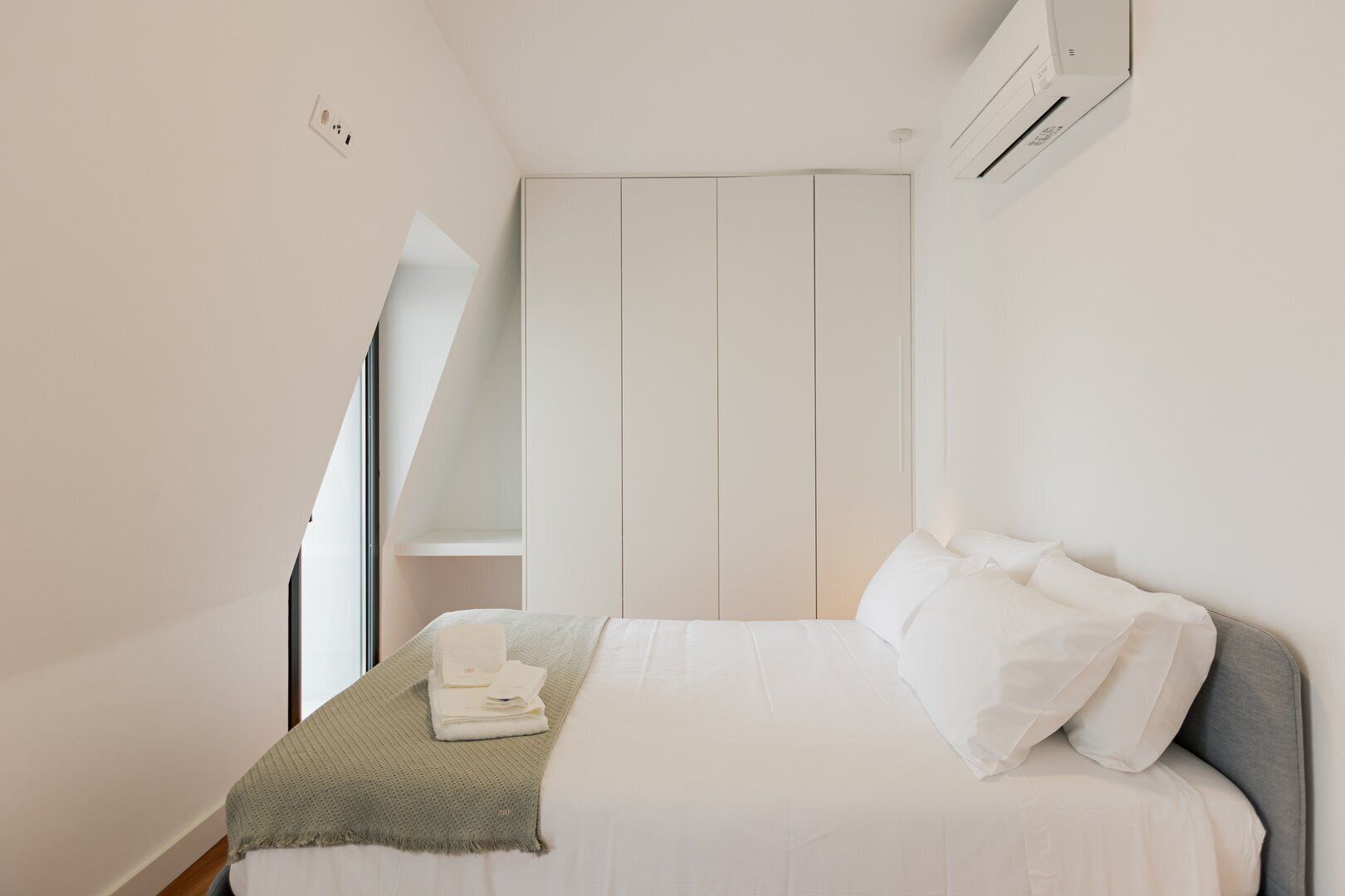 A bedroom with a bed, a bedside table, a wall-mounted air conditioner, and a wardrobe.