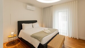 A modern bedroom with a bed, bedside table, and a large window with curtains.