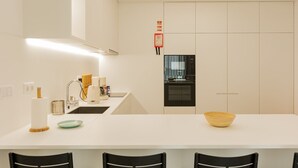 A modern kitchen with a white countertop, black chairs, a wooden bowl, and a built-in oven.