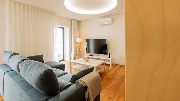 A modern living room with a grey sofa, a white coffee table, and a flat-screen TV on a white stand.