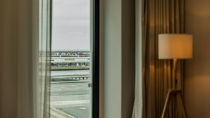 A hotel room with a large window overlooking a waterfront area, a lamp on the right, and a view of a building with signage.