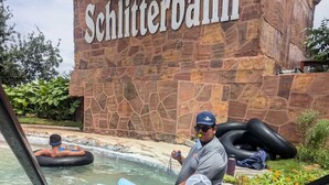 A water park with a stone wall labeled 'Schlitterbahn' and people floating on water tubes. - Rustic Retreat: Tub, Firepit, Porch Swings & Pool (San Marcos)