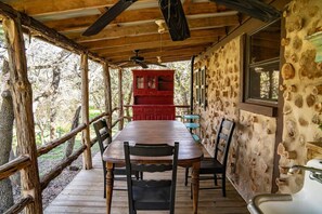 A rustic wooden dining area with a table and chairs, a red cabinet, and a stone wall with embedded logs.