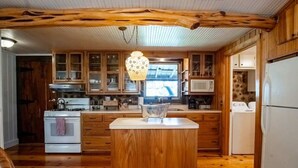 A kitchen with wooden cabinets, a central island, a stove, a microwave, and a refrigerator. - Rustic Retreat: Tub, Firepit, Porch Swings & Pool (San Marcos)