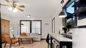 A modern living room with a sofa, coffee table, and a dining area. There is a kitchen with a sink and a refrigerator. - Outpost Vibes: Outhouse, Outdoor Shower & Pool (San Marcos)
