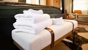 A neatly folded stack of white towels on a bench with a brown strap, in a room with a bed and a chair in the background. - Outpost Vibes: Outhouse, Outdoor Shower & Pool (San Marcos)