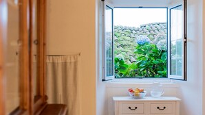 Un baño con vista a zonas verdes y un lavabo blanco con un frutero y una jarrón de vidrio.