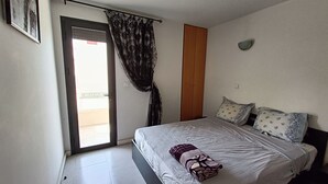 Un dormitorio con cama, armario de madera, puerta que da a un balcón y una lámpara fijada a la pared.