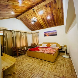 A bedroom with a wooden ceiling, a bed with a red bedspread, a desk, and a chair. - Hotel Jamla Regency Manali (Manali)