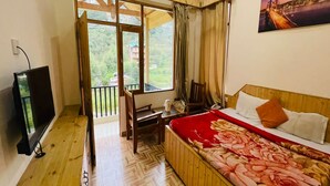 A bedroom with a bed, a TV, a wooden floor, a balcony with a view, and a painting on the wall. - Hotel Jamla Regency Manali (Manali)