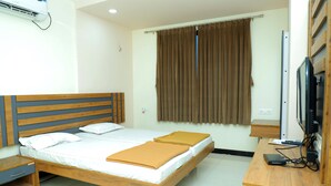 A double bed with a wooden headboard, a bedside table, a desk with a computer and a TV, and a window with curtains. - Hotel Anjani  (Latur)
