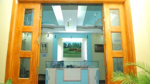 A reception area with a glass desk, framed artwork on the wall, and a ceiling fan. - Hotel Anjani  (Latur)
