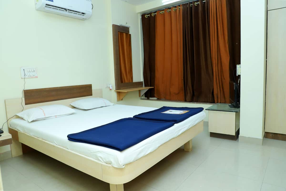 A single bed with white bedding and blue blankets, a bedside table, a mirror, and a window with brown curtains.