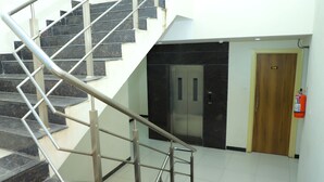 A staircase with metal railings leading to a room with a wooden door and a fire extinguisher mounted on the wall. - Hotel Anjani  (Latur)