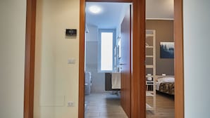 Une chambre d’hôtel avec un plancher en bois, un lit, un bureau et une salle de bain visible à travers une porte ouverte.