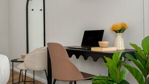 A modern room with a bed, a desk with a laptop, a chair, a small table with a candle, a vase with flowers, and a large plant. - Neighbourgood First Crescent (Cape Town)