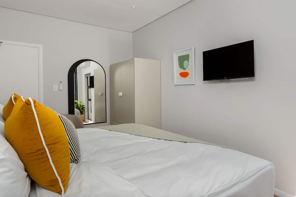 Une chambre d’hôtel moderne équipée d’un lit, d’un téléviseur à écran plat, d’une armoire et d’un miroir.