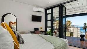 A modern bedroom with a bed, a TV, and a view of the ocean. - Neighbourgood First Crescent (Cape Town)
