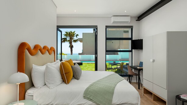A modern bedroom with a large bed, a desk, and a view of the outdoors. - Neighbourgood First Crescent (Cape Town)
