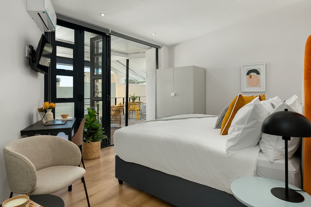 Une chambre moderne avec un grand lit, un bureau avec une chaise, une petite table et une plante en pot.