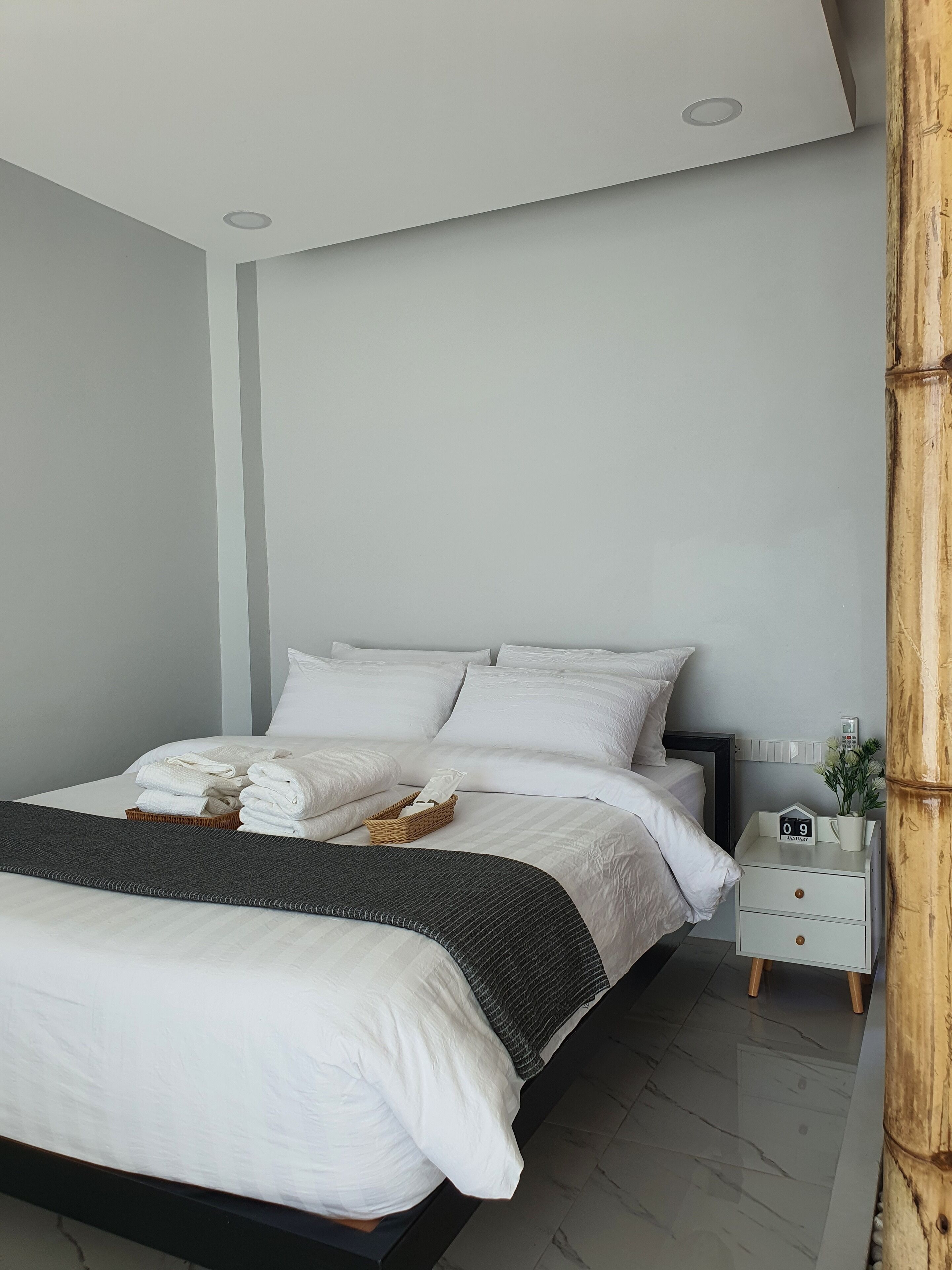 A modern bedroom with a large bed, white bedding, a bedside table with a clock, and a nightstand with a plant.