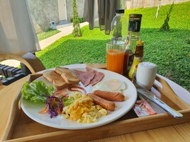 A breakfast tray with toast, ham, eggs, sausages, and a salad on a wooden table with a view of a garden.