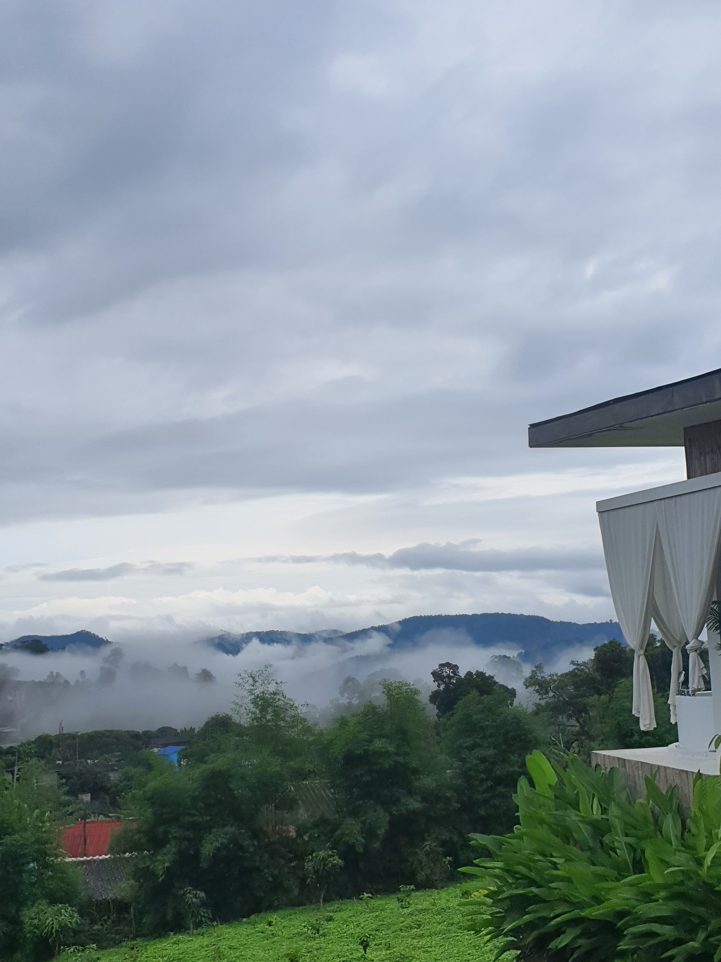 A view of a mountainous landscape with clouds, a building with a white facade, and lush greenery.