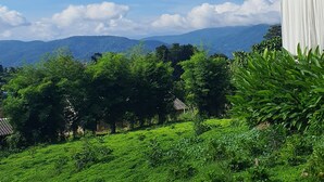A lush green landscape with a clear blue sky, a white building with a balcony, and distant mountains. - Cherpue Chiangmai (Mae Taeng)