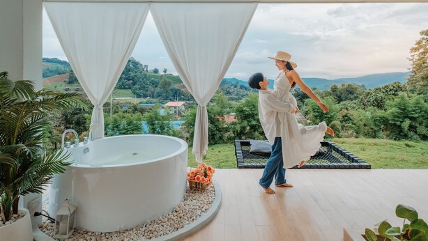 A modern bathroom with a large bathtub, a view of a lush landscape, and a couple in a white dress and suit. - Cherpue Chiangmai (Mae Taeng)