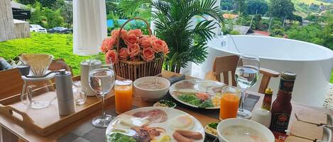 A dining table set with plates of food, drinks, and condiments, overlooking a scenic landscape.