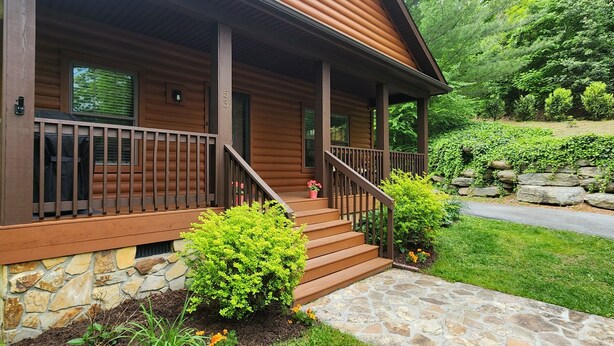 Une cabane en bois avec des fondations en pierre, une véranda dotée d’une balustrade et un chemin en pierre menant à l’entrée.