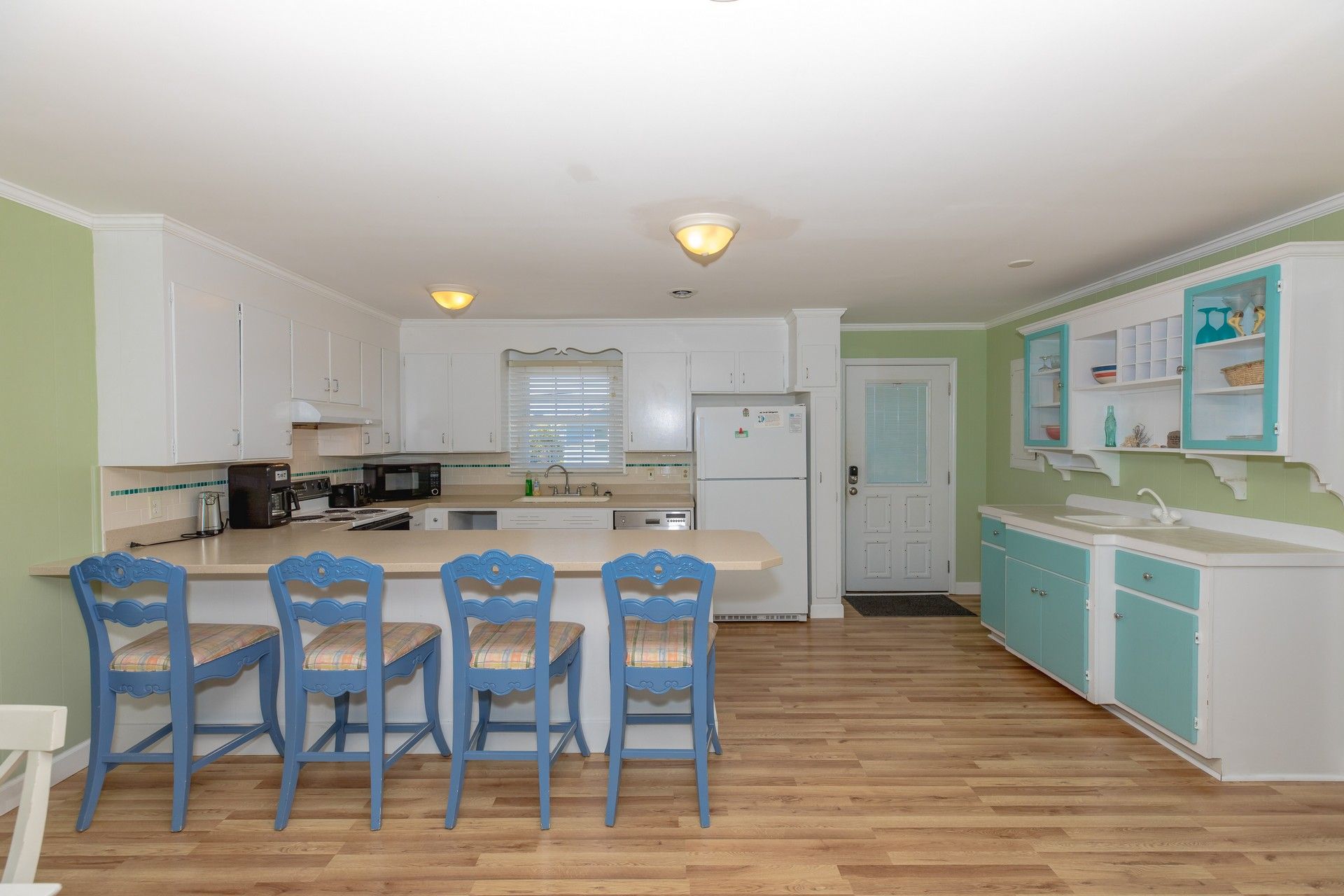 A kitchen with white cabinets, a central island with bar stools, a refrigerator, and a microwave.