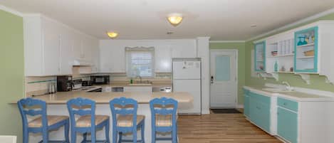 A kitchen with white cabinets, a central island with bar stools, a refrigerator, and a microwave.